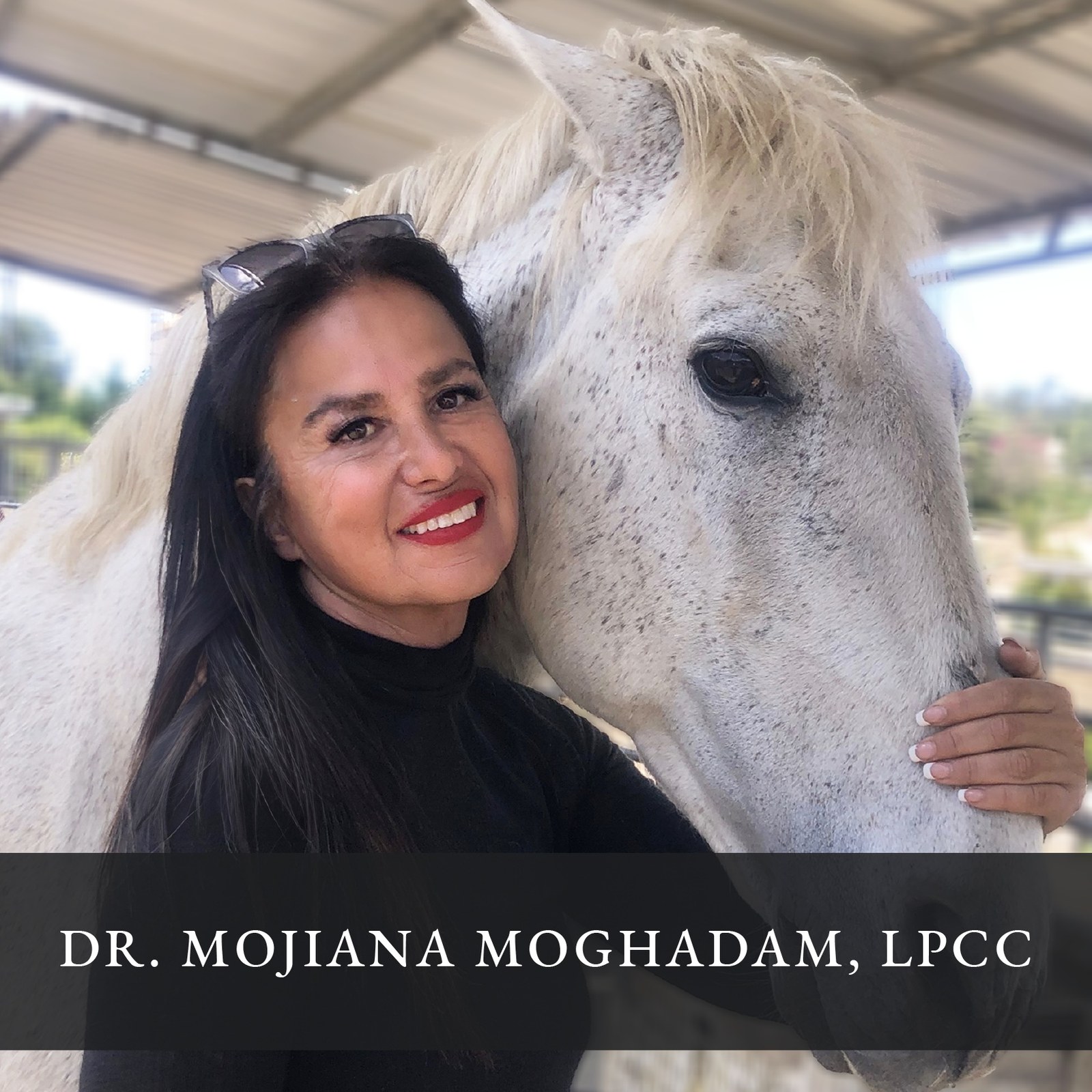 Dr. Mojiana Moghadam smiling beside a white horse.